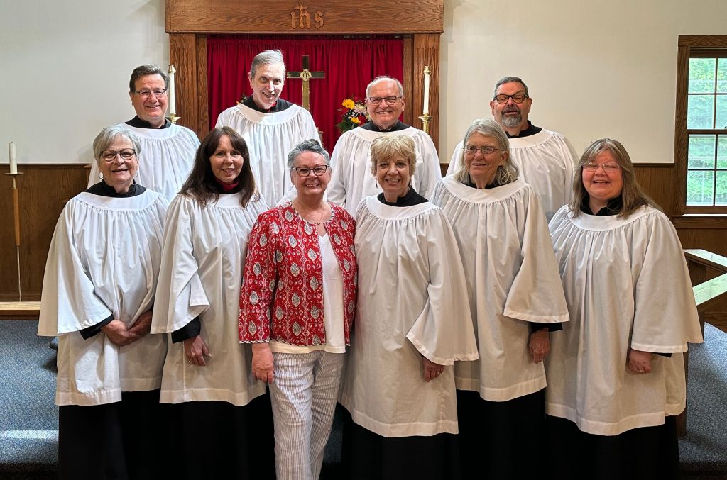 A group shot of the 2025 Trinity Choir in full Anglican vestments standing in front of the altar