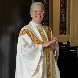 Photo of Rev. Johanna Marcure in white vestments standing in her former parish narthex